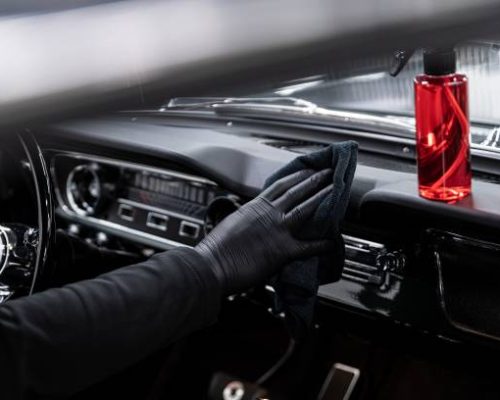 Employee of a car wash or a car detailing studio cleans the cockpit of a classic car.