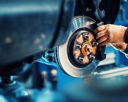 Closeup of unrecognizable mechanic replacing car brake pads. The car is lifted with hydraulic jack at eye level.